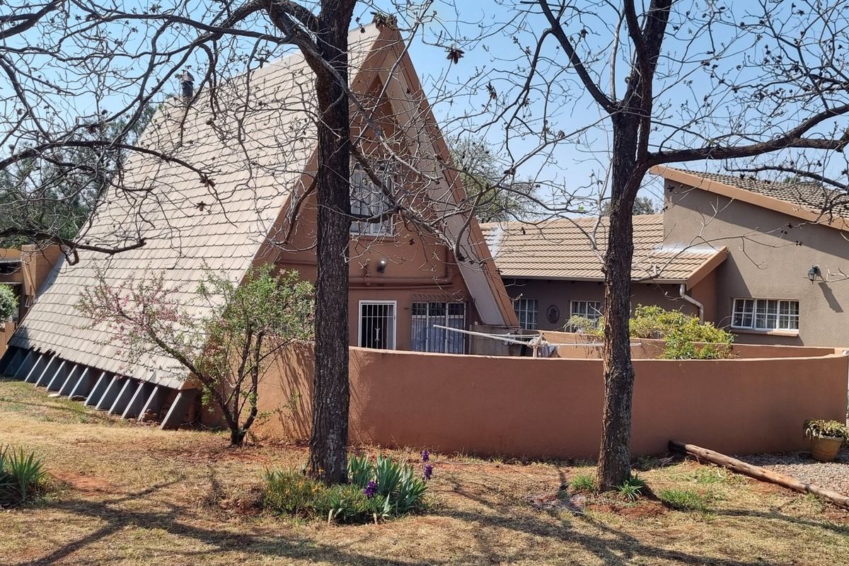 Rear view of a unique A-frame architectural structure with a surrounding boundary wall and mature trees on the property grounds.