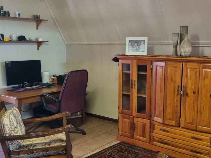 A functional home office space featuring tiled flooring, sloped ceilings, and built-in wall shelving, providing a practical area for work or study.