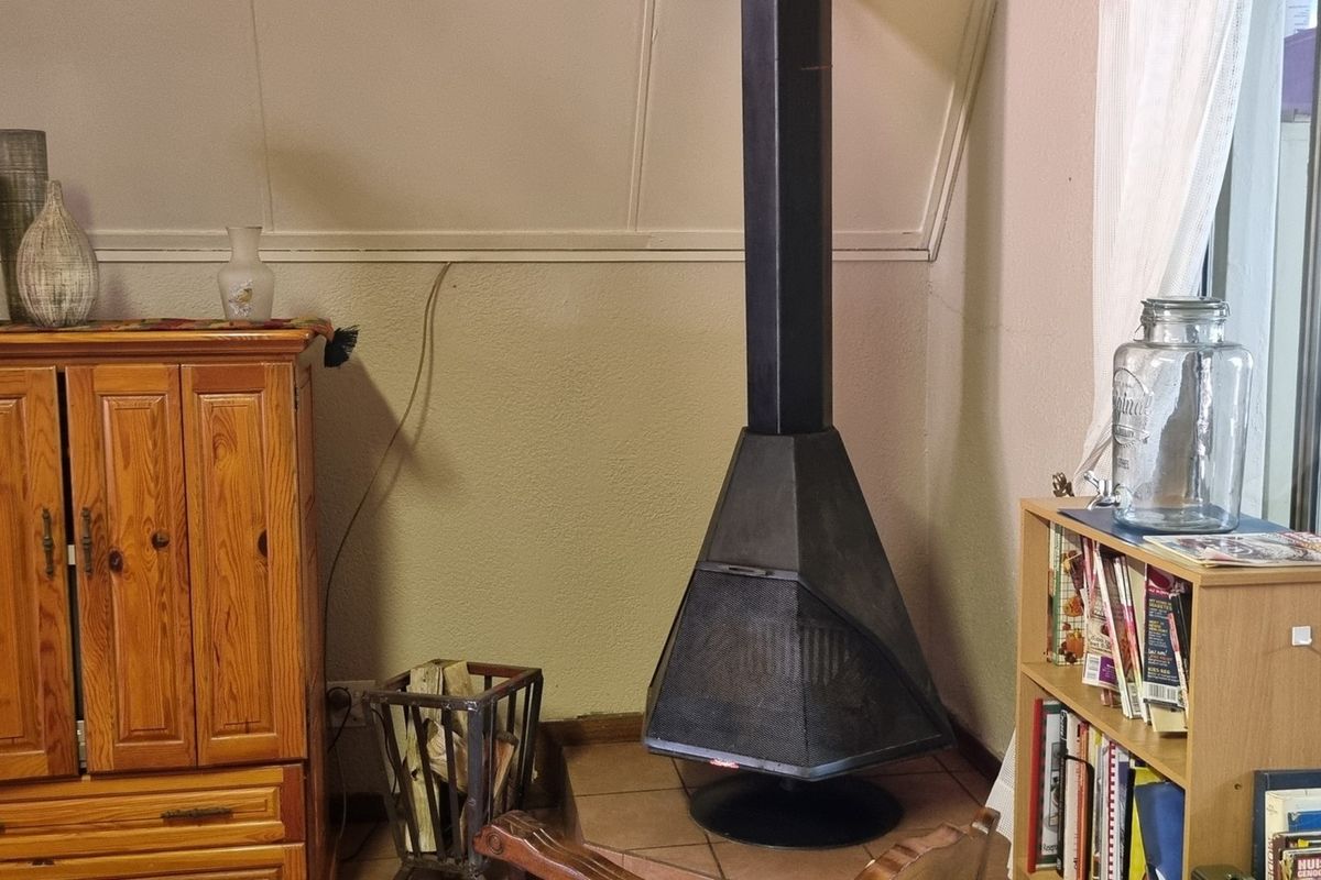 A living room area featuring a prominent black metal freestanding fireplace set on a tiled hearth against a sloped wall.