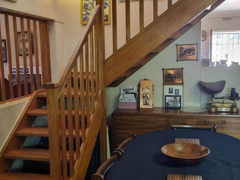 Open plan living area featuring a prominent wooden staircase with balustrade, tiled flooring, and access to the kitchen area.