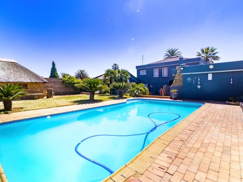 Outdoor pool area featuring a swimming pool, brick paved surround, and a traditional thatched lapa in the garden.