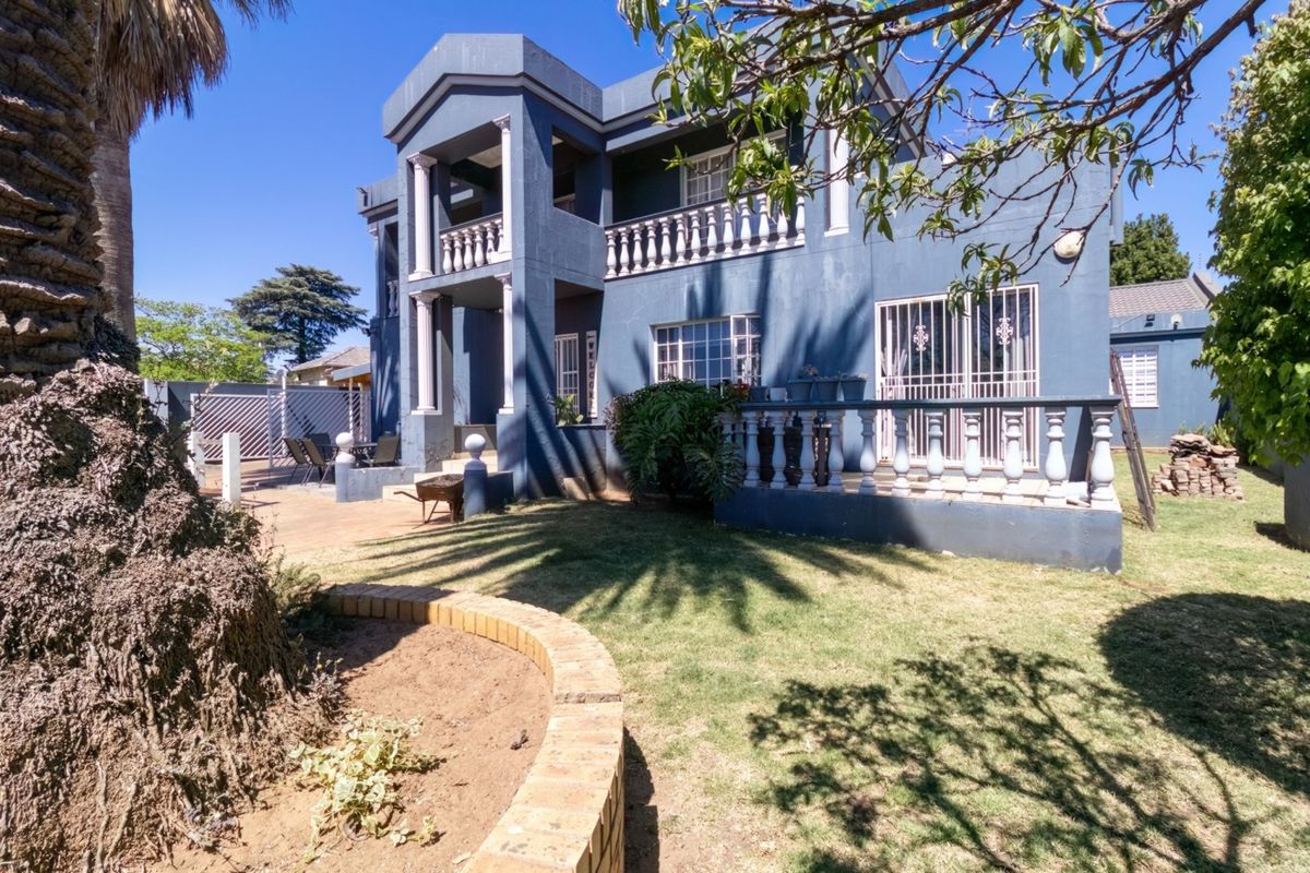 Rear view of a two-story house featuring a balcony with balustrades, a paved patio area, and a landscaped garden with a brick retaining wall.