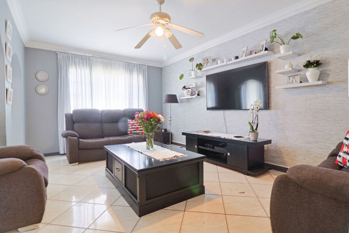 A well-maintained living room featuring tiled flooring, crown molding, and a central ceiling fan, creating a comfortable and functional family space.