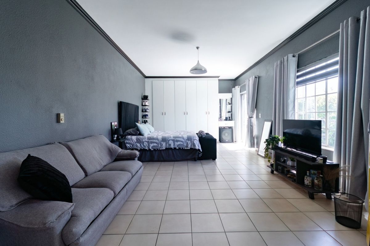 Spacious bedroom featuring tiled flooring, built-in cupboards, and crown molding, offering a comfortable and well-maintained living space.