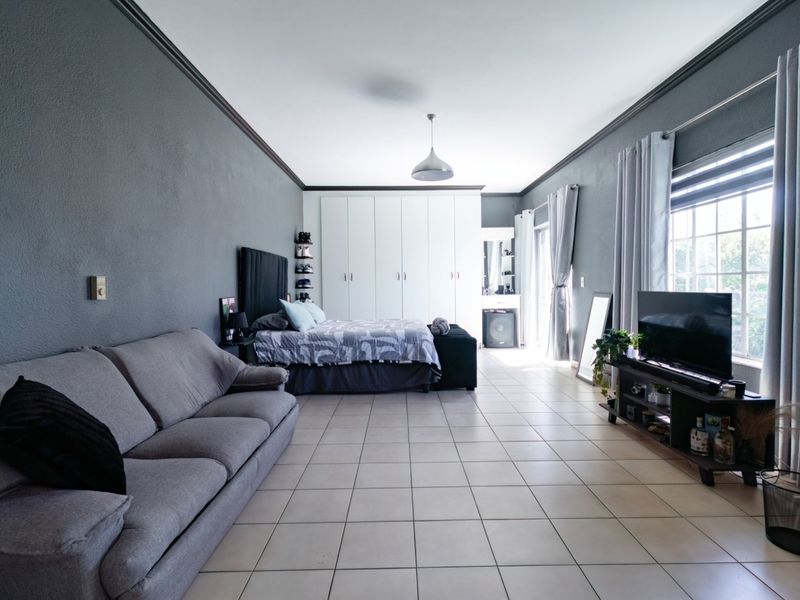 Spacious bedroom featuring tiled flooring, built-in cupboards, and crown molding, offering a comfortable and well-maintained living space.