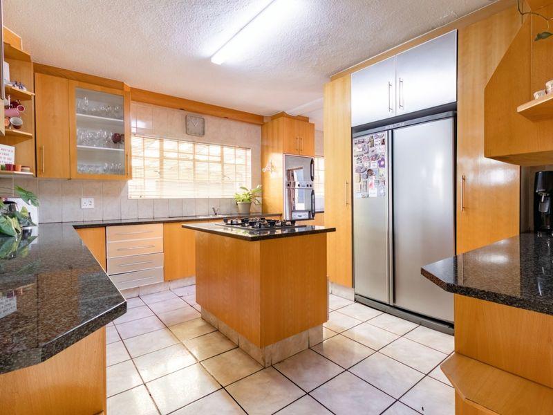 A functional kitchen featuring wooden cabinetry, granite countertops, a central island with a gas hob, and tiled flooring.