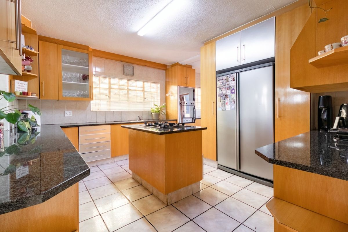 A functional kitchen featuring wooden cabinetry, granite countertops, a central island with a gas hob, and tiled flooring.