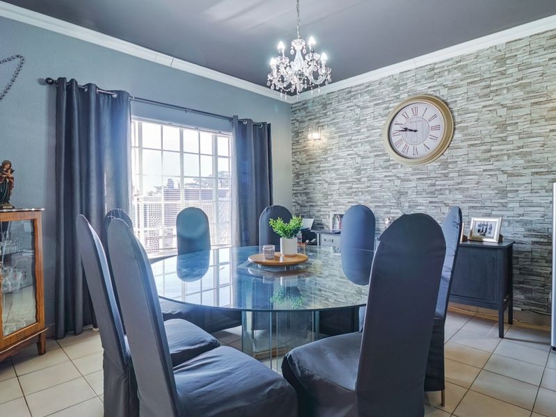 A well-maintained dining room featuring a stone veneer accent wall, tiled flooring, crown molding, and an elegant crystal chandelier.