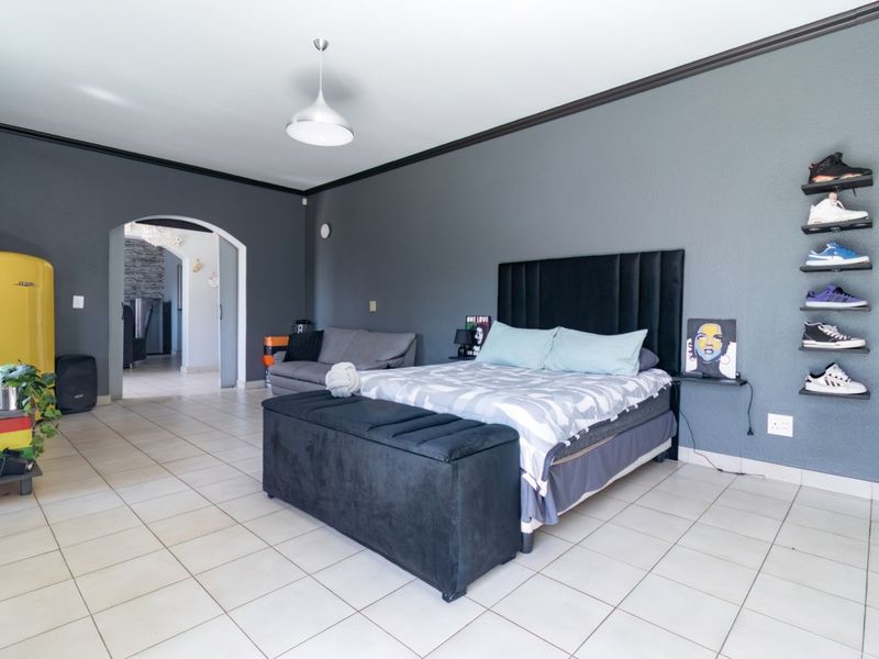 Spacious bedroom featuring tiled flooring, dark grey accent walls, crown molding, and an arched doorway leading to an adjacent living area.