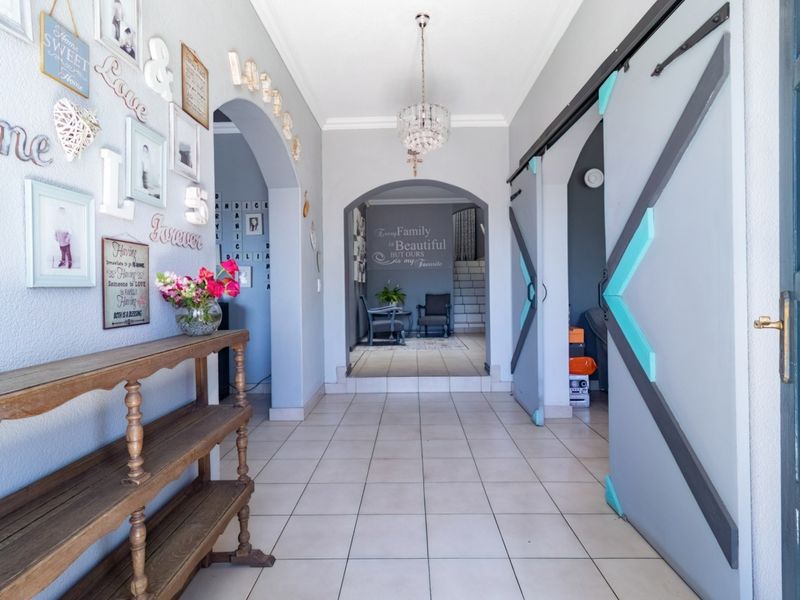 A bright, tiled hallway featuring an elegant crystal chandelier, arched transitions, and a modern sliding barn door leading to adjacent living spaces.