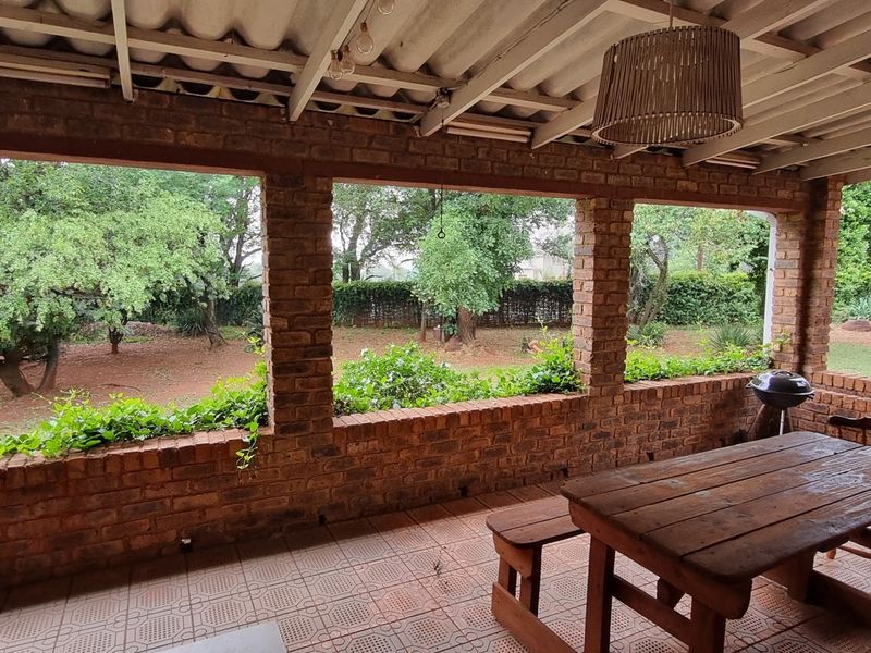Covered outdoor patio featuring exposed brick pillars, tiled flooring, and built-in brick planter boxes, overlooking a spacious garden area.
