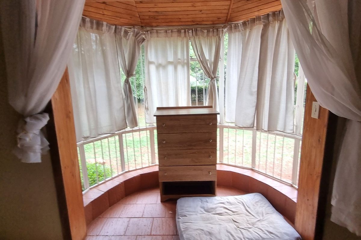A bedroom featuring a bay window with timber ceiling accents and tiled flooring, providing natural light and garden views.