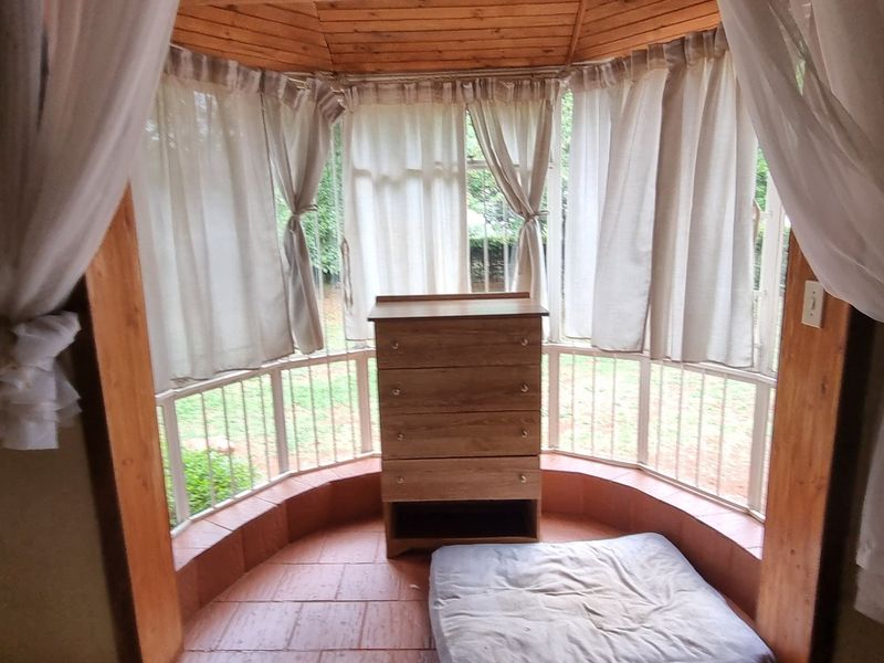 A bedroom featuring a bay window with timber ceiling accents and tiled flooring, providing natural light and garden views.