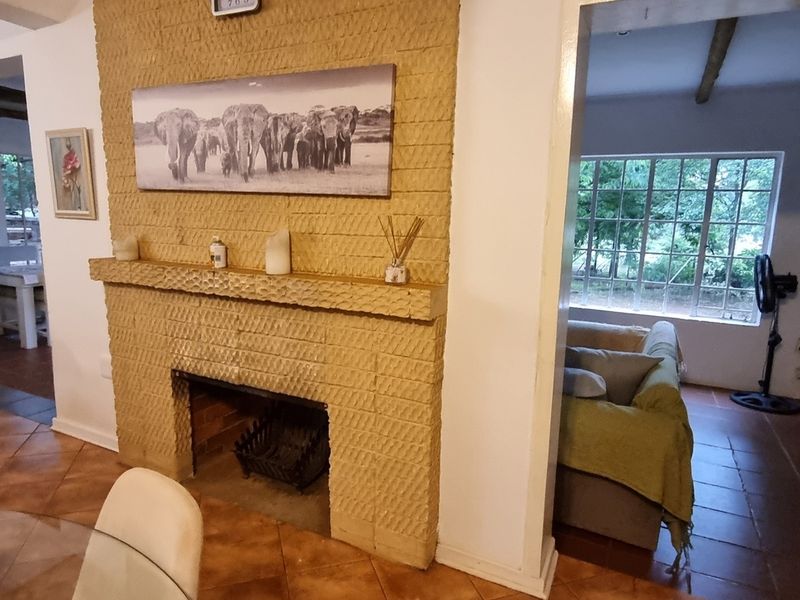 Living area featuring a prominent textured brick fireplace, tiled flooring, and large windows providing natural light and garden views.