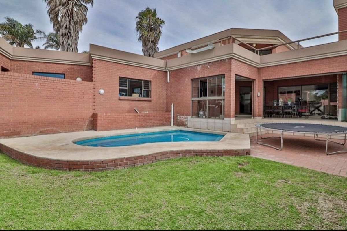 Rear exterior view featuring a swimming pool, paved patio area, and a multi-level brick house with sliding door access to the living space.