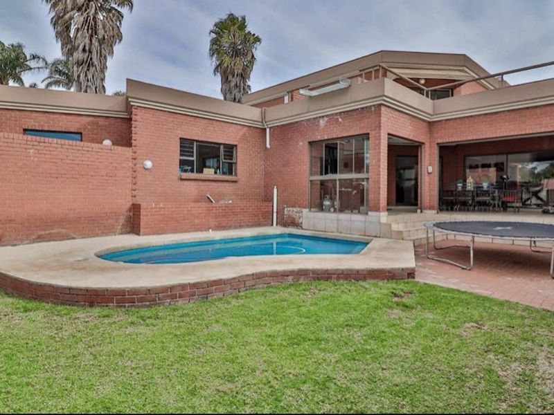 Rear exterior view featuring a swimming pool, paved patio area, and a multi-level brick house with sliding door access to the living space.