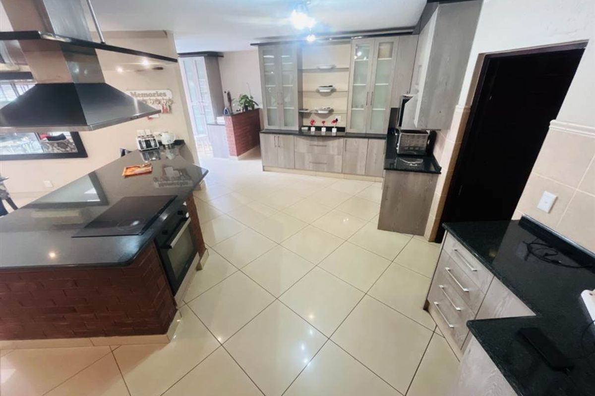 Modern kitchen featuring granite countertops, built-in oven, electric hob, stainless steel extractor fan, and ample cabinetry with tiled flooring.