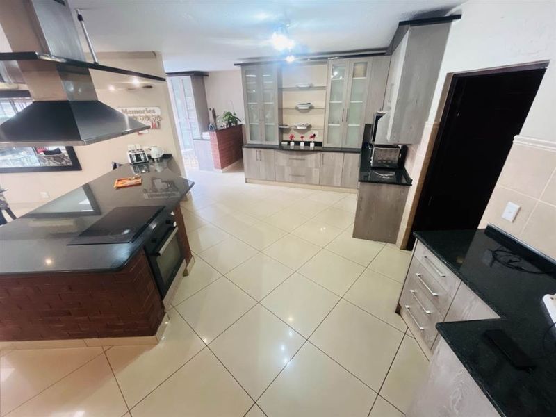 Modern kitchen featuring granite countertops, built-in oven, electric hob, stainless steel extractor fan, and ample cabinetry with tiled flooring.