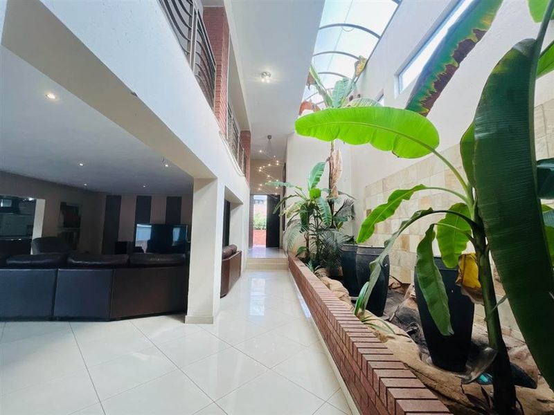Spacious double-volume hallway featuring a large skylight, tiled flooring, and an integrated brick planter box, creating a bright and airy transition space.