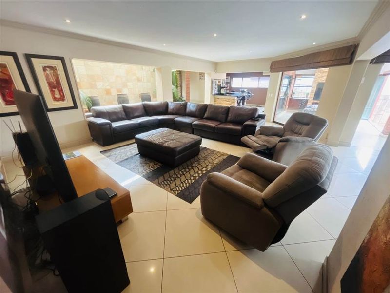 Spacious open-plan living area featuring tiled floors, recessed lighting, and a stone feature wall, seamlessly connecting to the kitchen and outdoor patio space.