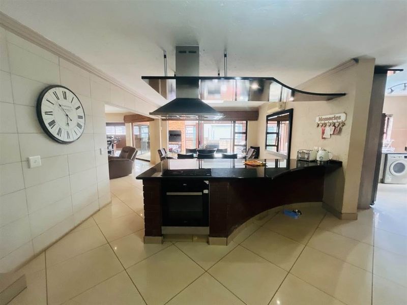Open plan living area featuring a central kitchen island with built-in oven, cooktop, and extractor fan, leading to a bright dining space with sliding doors.