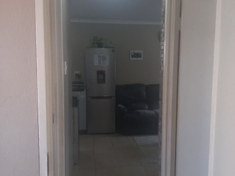 A view through a doorway into an open plan living and kitchen area with tiled flooring and neutral wall finishes.