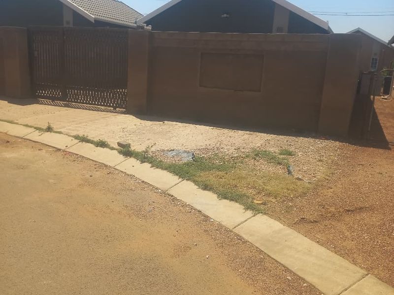 Front view of the property featuring a perimeter wall, metal driveway gate, and tiled roof structure.