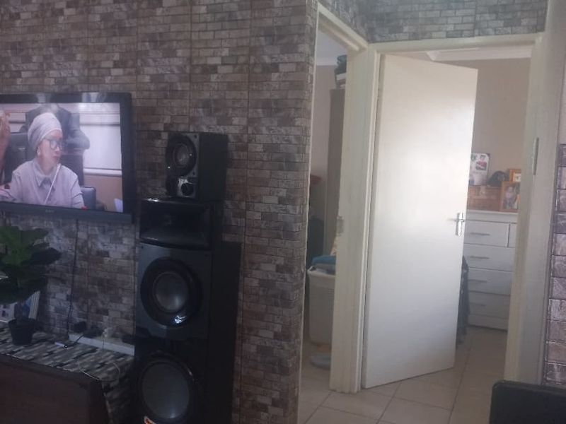 Living area featuring tiled flooring and decorative brick-effect wall cladding, with an open doorway leading to an adjacent room.