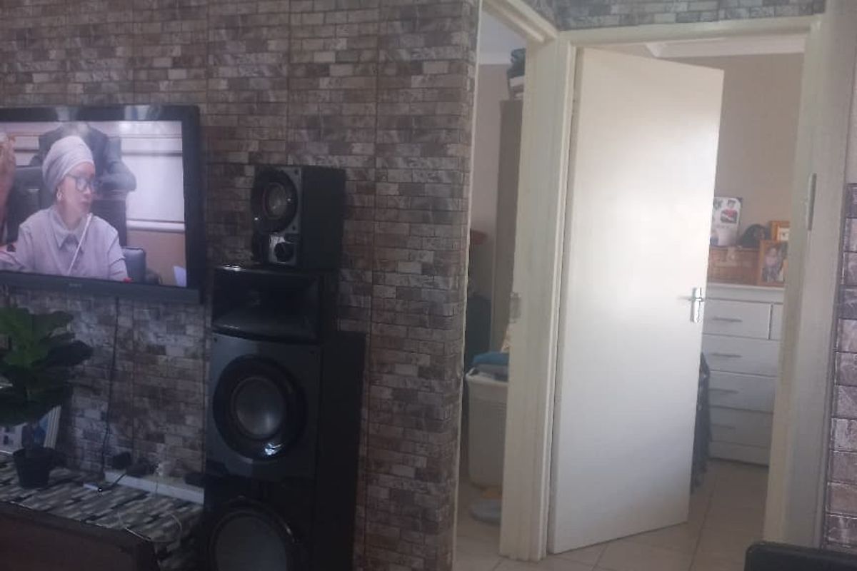 Living area featuring tiled flooring and decorative brick-effect wall cladding, with an open doorway leading to an adjacent room.
