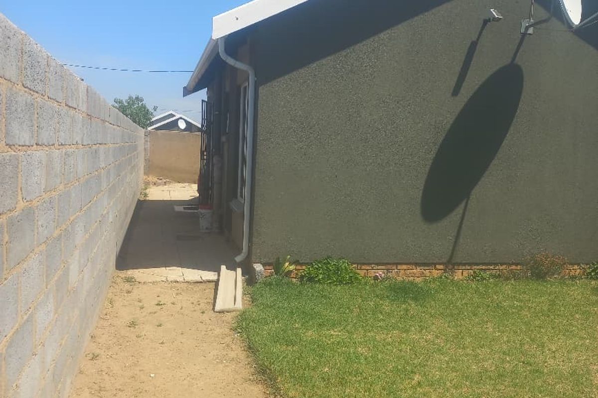 A view of the rear exterior of the house featuring a boundary wall, lawn, and satellite dish installation.