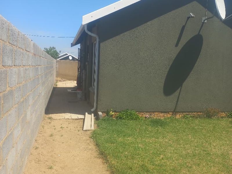 A view of the rear exterior of the house featuring a boundary wall, lawn, and satellite dish installation.