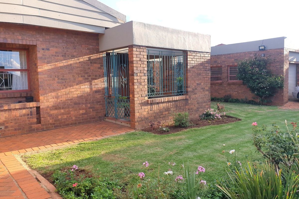A well-maintained face brick exterior featuring a covered entrance with security bars, a paved walkway, and a neat landscaped garden.
