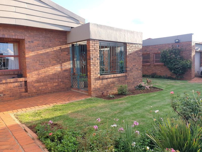 A well-maintained face brick exterior featuring a covered entrance with security bars, a paved walkway, and a neat landscaped garden.