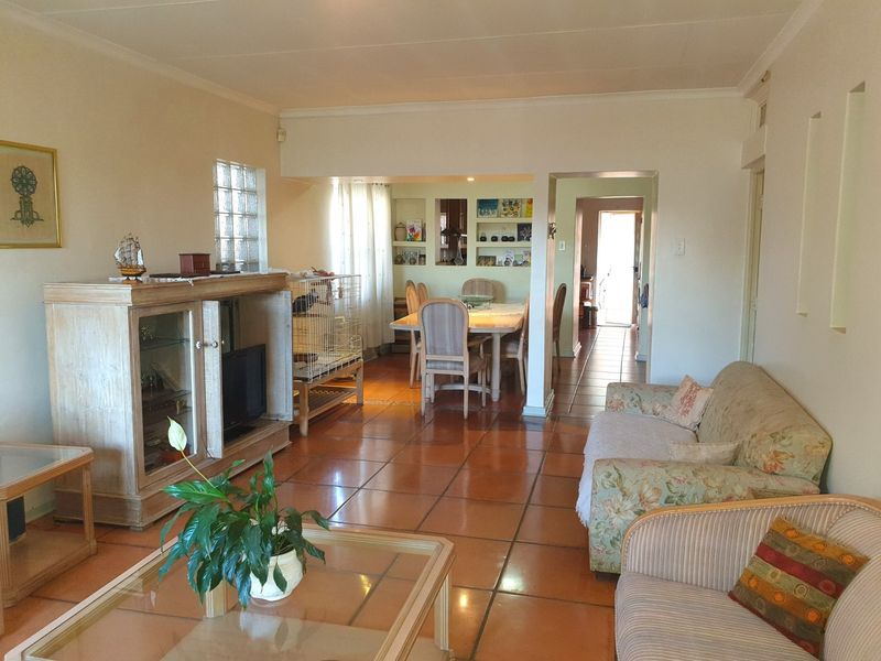 Open plan living and dining area featuring terracotta floor tiles, built-in display shelving, and a glass block window, offering a functional layout.