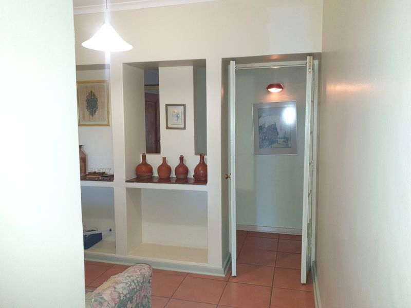 A hallway featuring built-in wall shelving, terracotta-style floor tiles, and a doorway leading to an adjacent room.