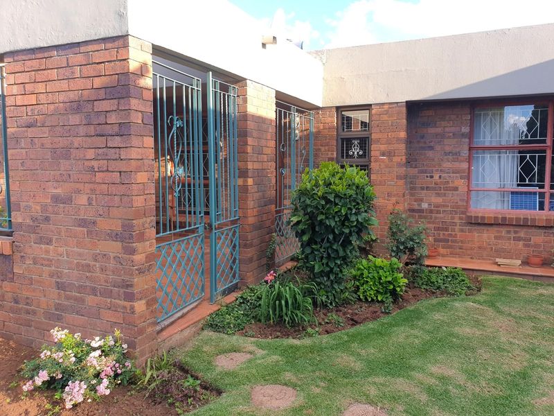 A rear view of the property featuring a face brick facade, a small tiled patio area with security gates, and a well-maintained garden.