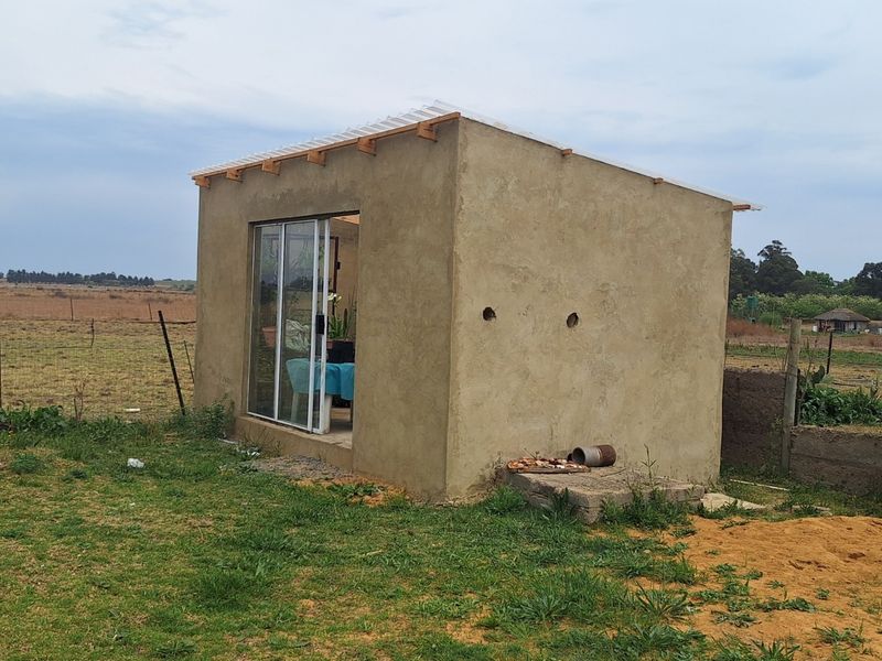 A small, detached utility structure with cement plaster walls and a sliding glass door, situated on a rural small holding.