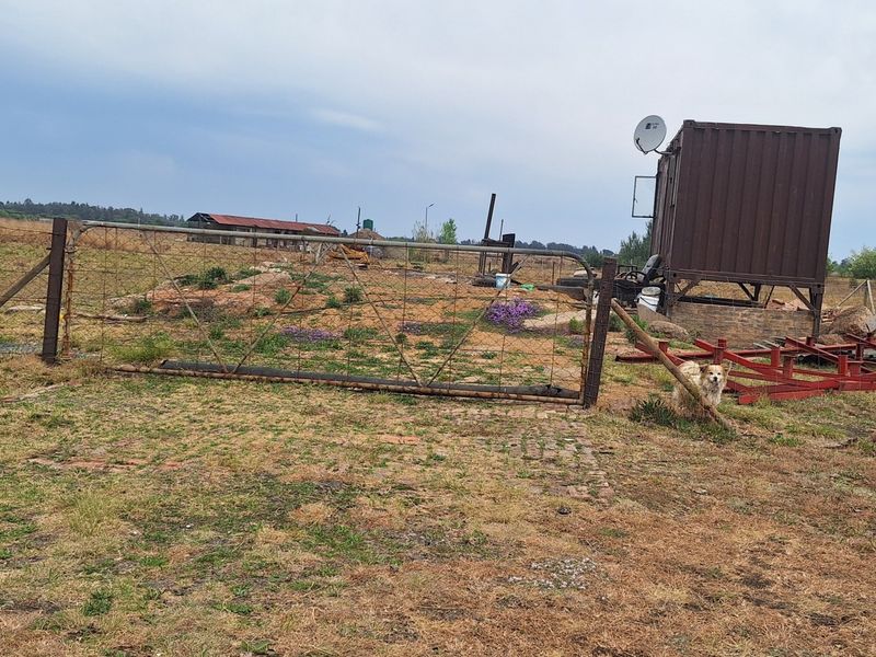 An expansive outdoor area on a small holding featuring wire fencing, a metal gate, and a shipping container structure.