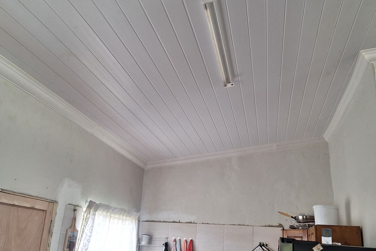 A kitchen area featuring a tongue and groove ceiling with coving and tiled splashbacks, currently requiring finishing touches to the wall plastering.