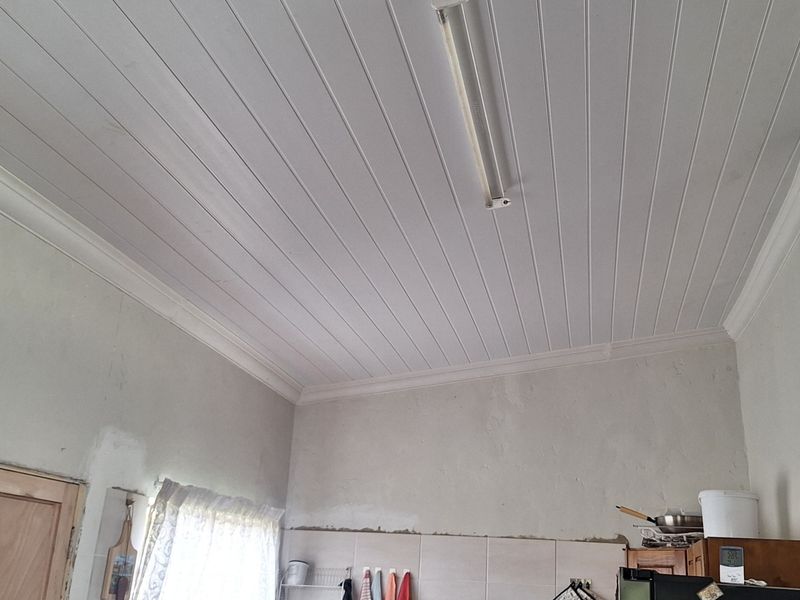 A kitchen area featuring a tongue and groove ceiling with coving and tiled splashbacks, currently requiring finishing touches to the wall plastering.