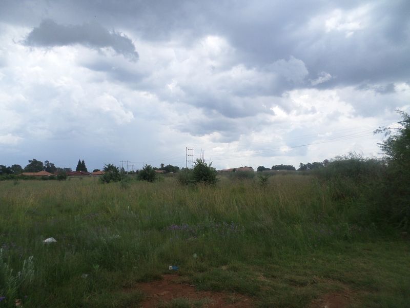 A view of a vacant residential plot featuring natural grass coverage and overhead power lines under a cloudy sky.