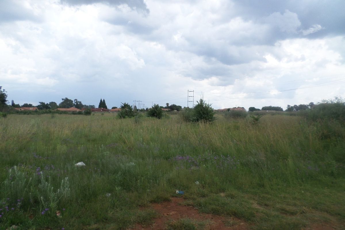 A view of a vacant residential plot featuring open grassland and overhead power lines under a cloudy sky.