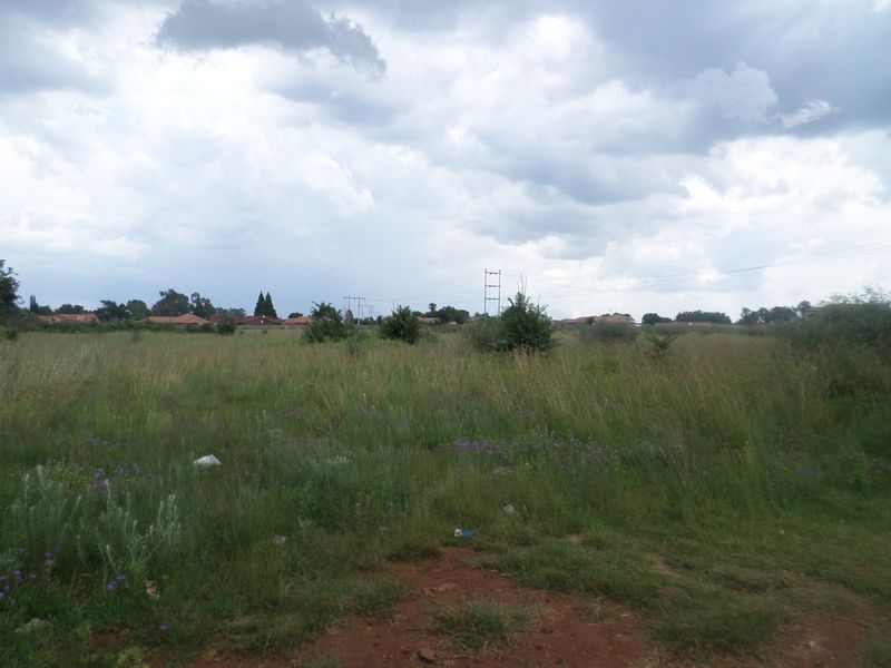 A view of a vacant residential plot featuring open grassland and overhead power lines under a cloudy sky.