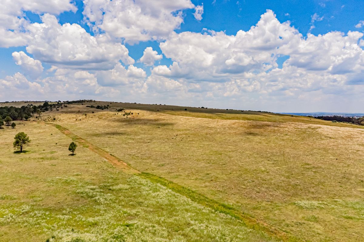 An aerial view of expansive, open farm land featuring natural grasslands and a dirt access track under a clear blue sky.