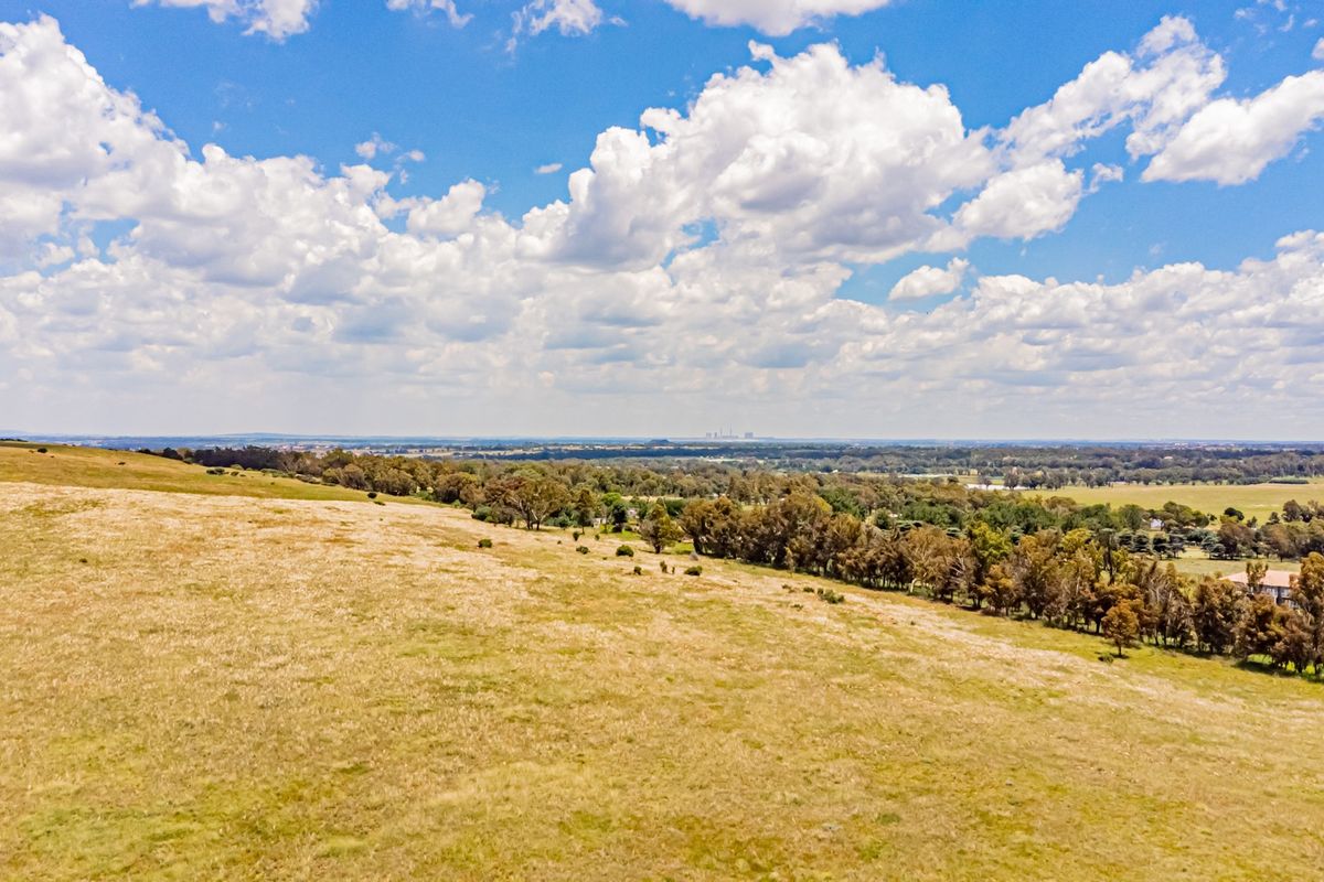 An aerial view of the expansive farm property featuring rolling pastures and established tree lines under a bright blue sky.