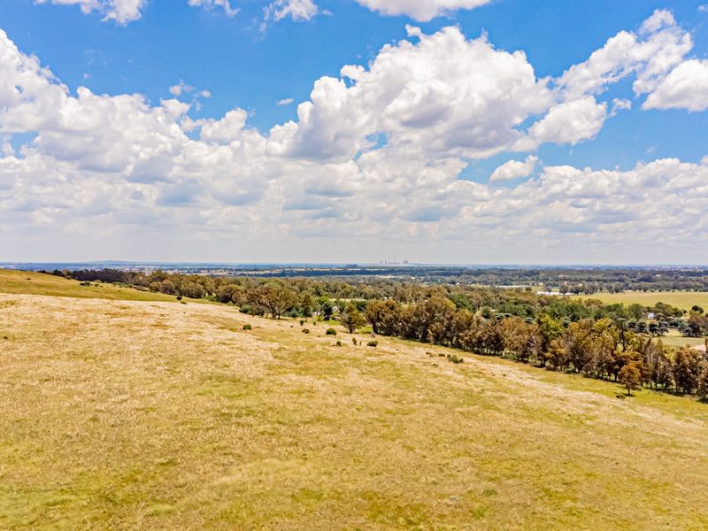 An aerial view of the expansive farm property featuring rolling pastures and established tree lines under a bright blue sky.
