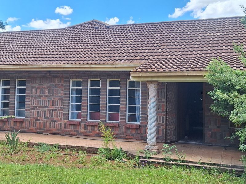Front elevation of a face-brick small holding residence featuring a covered patio, decorative column, and tiled roof, set within a garden area.