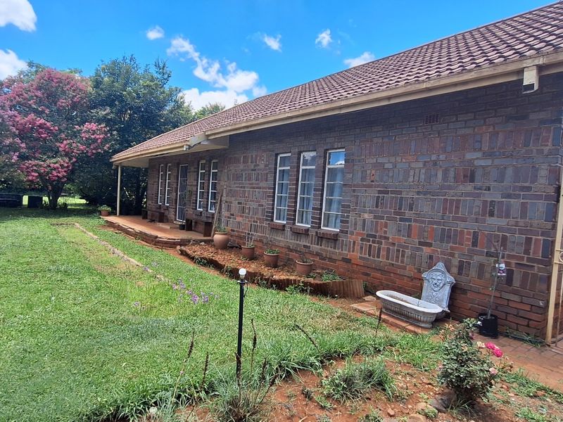 Rear view of a face-brick small holding dwelling featuring a tiled roof, covered patio area, and surrounding garden space.