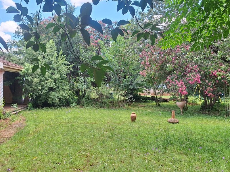 A lush, established garden area featuring a lawn, mature trees, and a view of the home's brick exterior and covered patio.