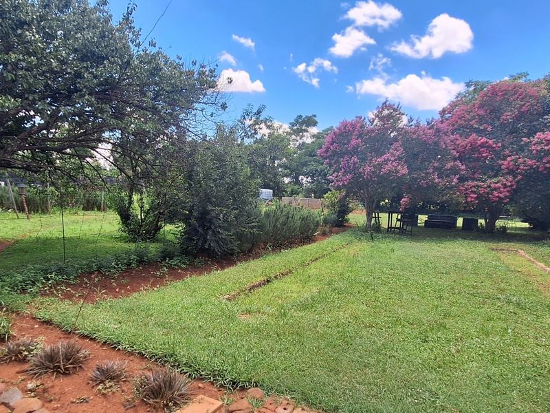 A well-maintained garden area featuring a lush lawn, mature trees, flowering shrubs, and a natural earthen pathway leading through the property grounds.